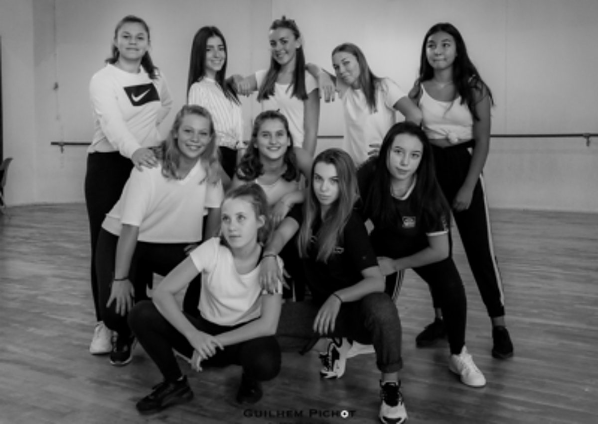 Photo en noir et blanc d'un groupe de jeunes filles posant ensemble dans une salle de danse avec une barre au mur.