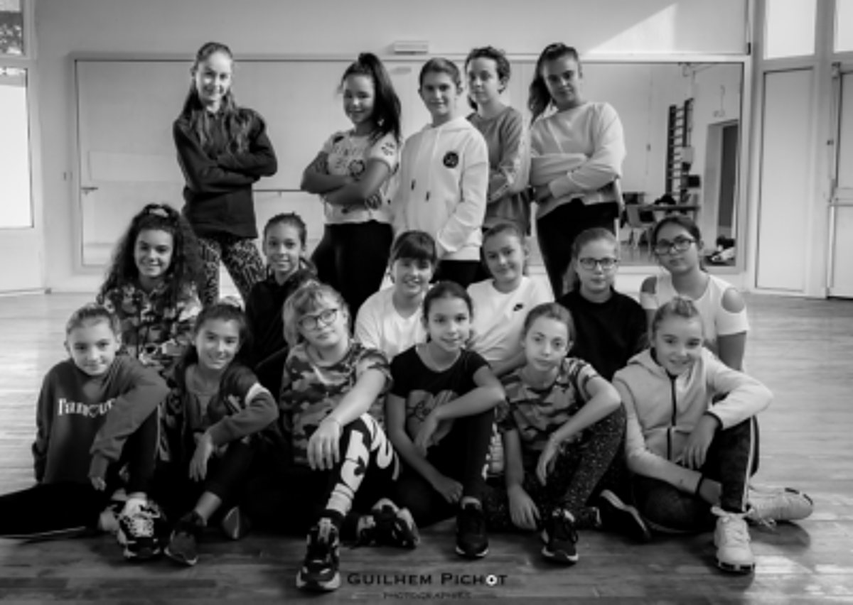 Photo en noir et blanc d'un groupe d'une quinzaine de jeunes filles posant, certaines debout et d'autres assises au sol, dans une salle de danse.