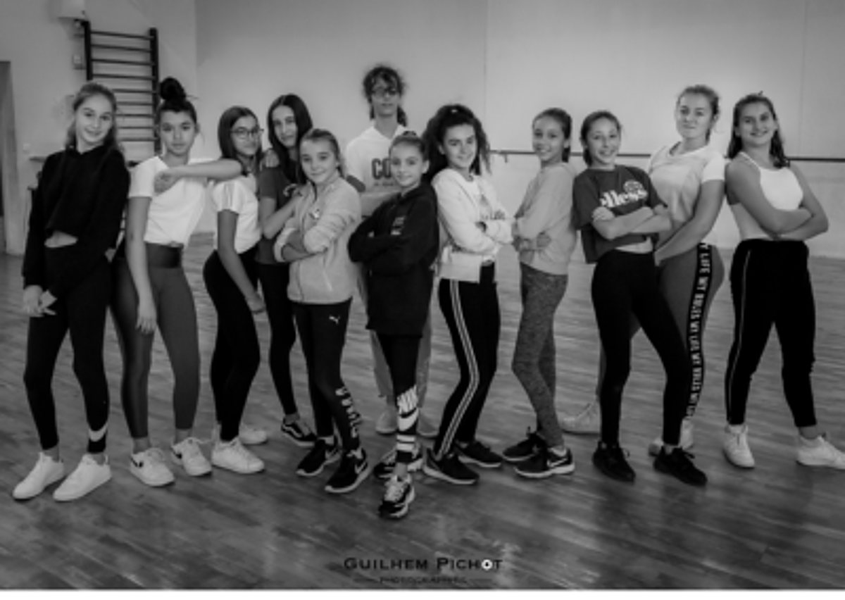 Photo en noir et blanc d'un groupe de jeunes filles en tenue de sport alignées côte à côte dans une salle de danse au parquet.