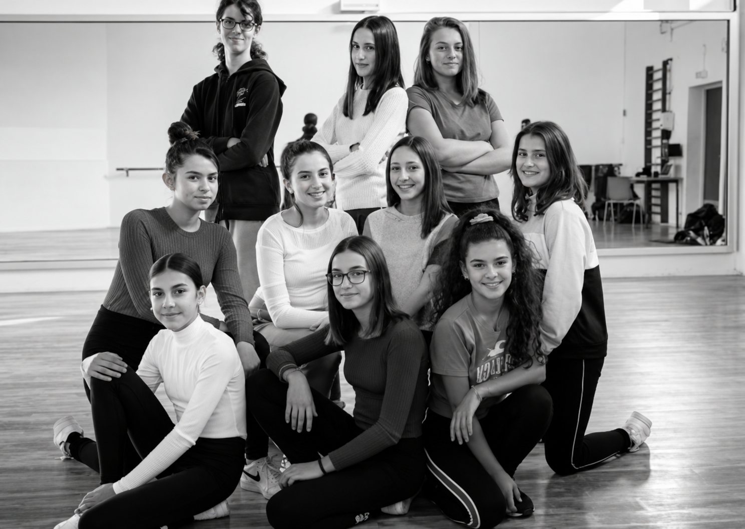 Photo en noir et blanc d'un groupe de jeunes filles posant ensemble devant un grand miroir dans une salle de danse.