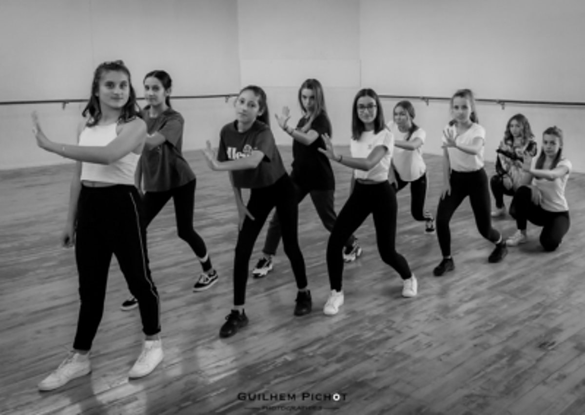 Photo en noir et blanc d'un groupe de jeunes filles en pose de danse sur le parquet d'un studio avec barre et miroir.
