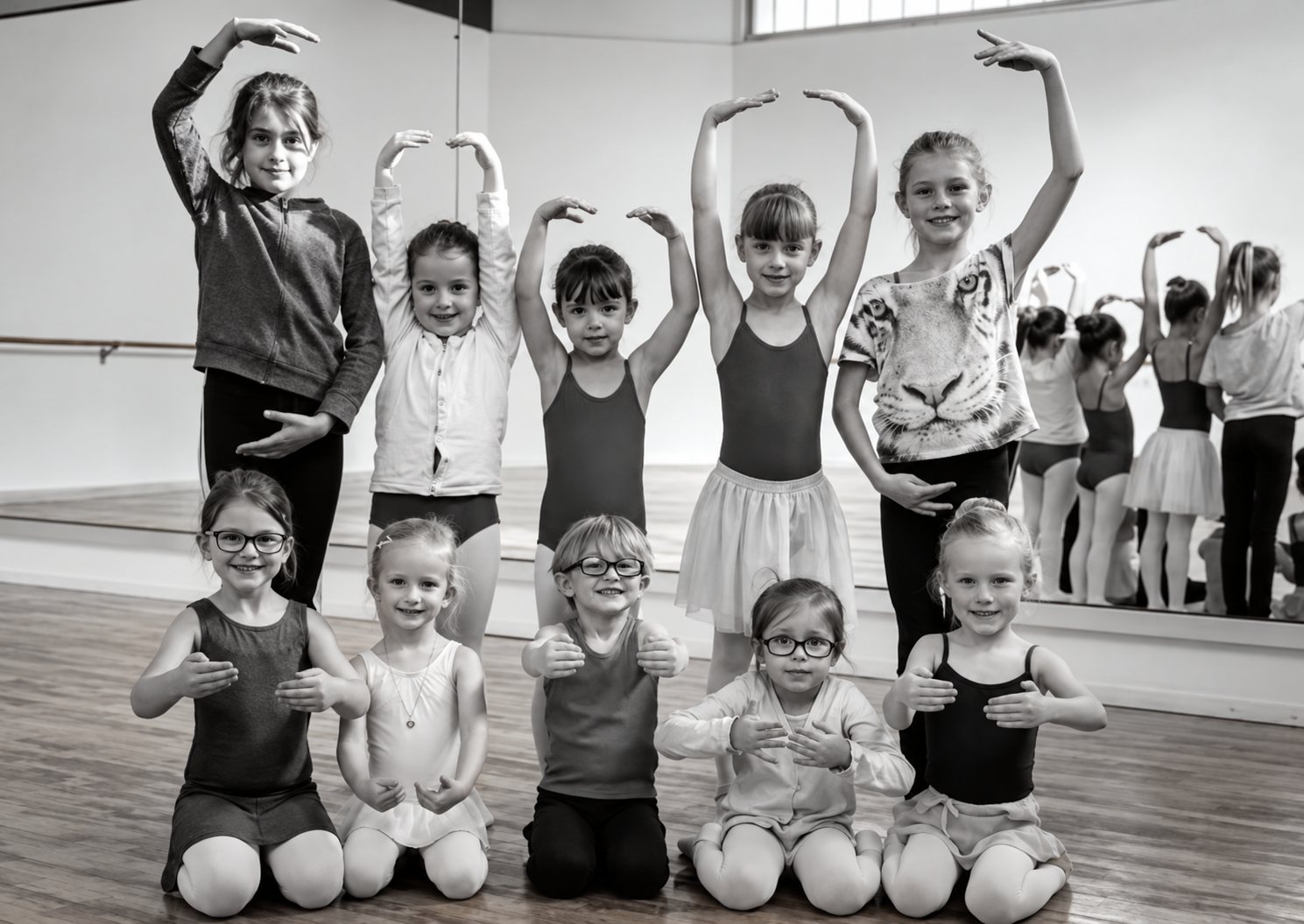 Des petites filles en tenue de danse posent en deux rangées dans un studio, les unes debout les bras arrondis au-dessus de la tête, les autres accroupies devant elles.