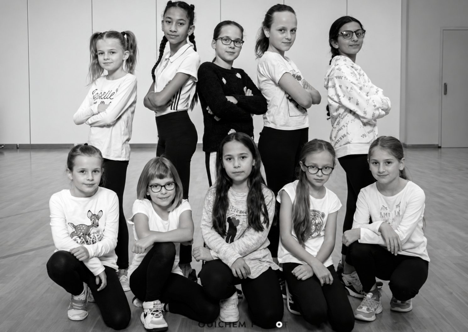 Photo en noir et blanc d'un groupe de neuf jeunes filles posant en deux rangées, certaines debout et d'autres accroupies, dans une salle de danse.